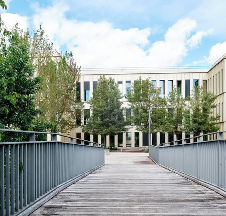 Manoir historique en pierre dans parc paysager avec pelouse, arbres et promeneurs.