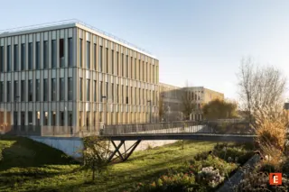 Complexe de bureaux et campus modernes avec pont piéton, façades verticales et espaces paysagers.