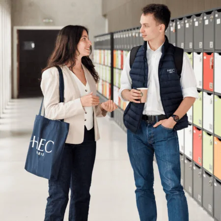 Couloir HEC Paris avec casiers colorés et deux étudiants discutant.