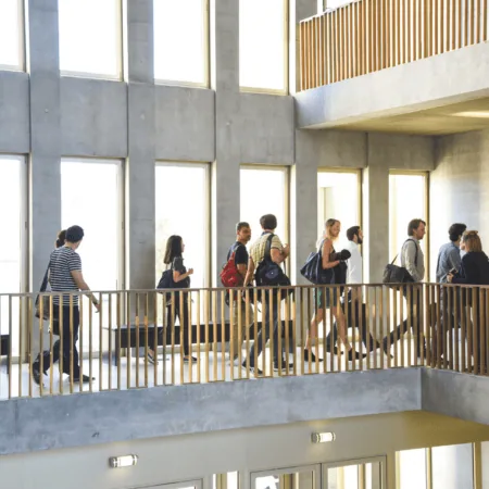Atrium lumineux moderne avec couloir, personnes en transit, béton et balustrade en bois.
