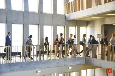 Atrium lumineux moderne avec couloir, personnes en transit, béton et balustrade en bois.