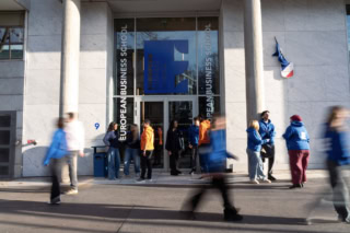 Entrée vitrée dune école de commerce, façade en marbre, étudiants groupés.