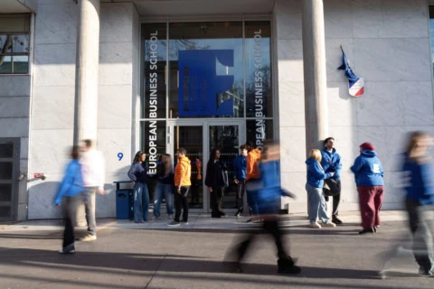 Entrée vitrée dune école de commerce, façade en marbre, étudiants groupés.