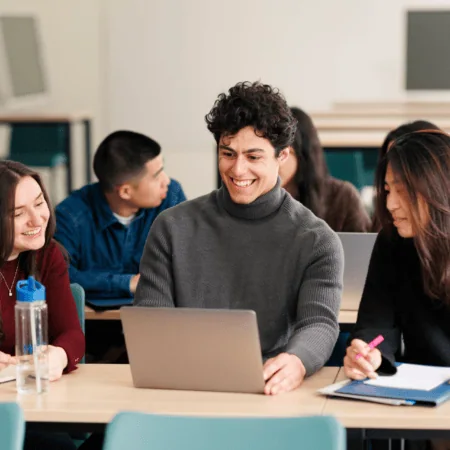 Étudiants en travail déquipe autour dun ordinateur portable dans une salle de classe moderne.