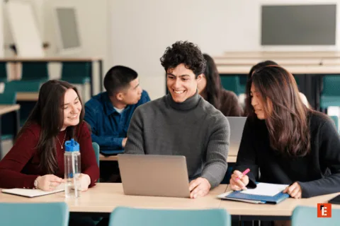 Étudiants en travail déquipe autour dun ordinateur portable dans une salle de classe moderne.