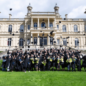 Cérémonie de remise de diplômes : diplômés en toques lançant leurs chapeaux devant bâtiment classique.