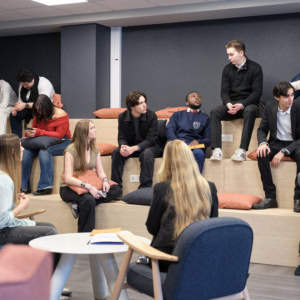Espace réunion contemporain avec gradins en bois, coussins terracotta, personnes en discussion.