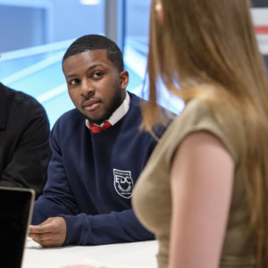 Étudiant attentif en entretien à table, discussion collaborative dans un cadre professionnel.