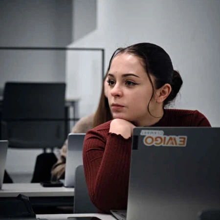 Étudiante attentive sur ordinateur portable en salle de cours, sticker visible.