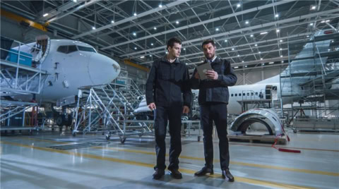 Hangar dentretien aéronautique, techniciens consultant une tablette près de fuselages davions.