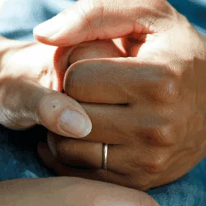 Deux mains jointes sur un lit d'hôpital.