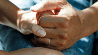 Deux mains jointes sur un lit d'hôpital.