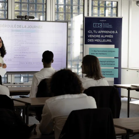 Salle de formation vente avec formateur, écran numérique et stagiaires attentifs.