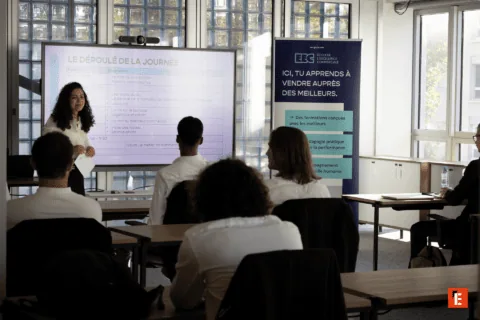 Salle de formation vente avec formateur, écran numérique et stagiaires attentifs.
