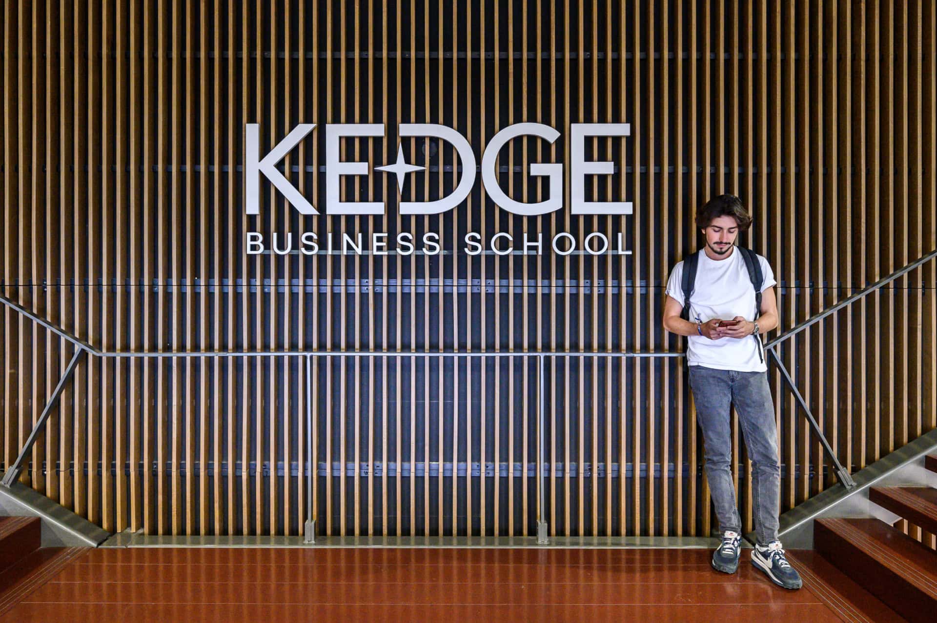 Un étudiant posant devant un mur avec le logo de KEDGE