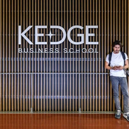 Un étudiant posant devant un mur avec le logo de KEDGE