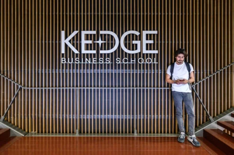 Un étudiant posant devant un mur avec le logo de KEDGE