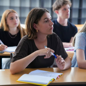 Étudiante concentrée en classe prenant des notes au stylo, cahier ouvert.