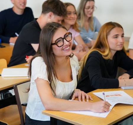 Étudiantes en cours prenant des notes, jeune femme souriante aux lunettes au premier plan.