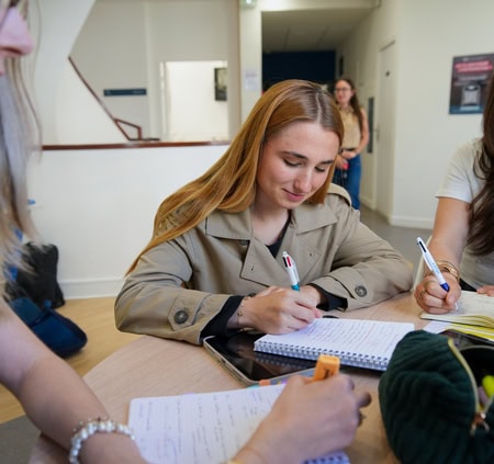 Étudiants en groupe autour dune table, prise de notes collaborative sur campus.