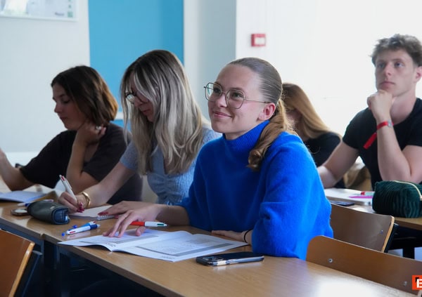 Étudiants en cours, prise de notes dans une salle de classe lumineuse.