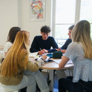 Étudiants en groupe détude autour dune table ronde, cahiers et collaboration dans une salle lumineuse.