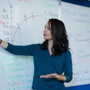 Professeure expliquant un graphique mathématique de statistiques sur tableau blanc pendant un cours.