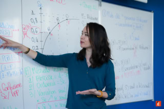 Professeure expliquant un graphique mathématique de statistiques sur tableau blanc pendant un cours.