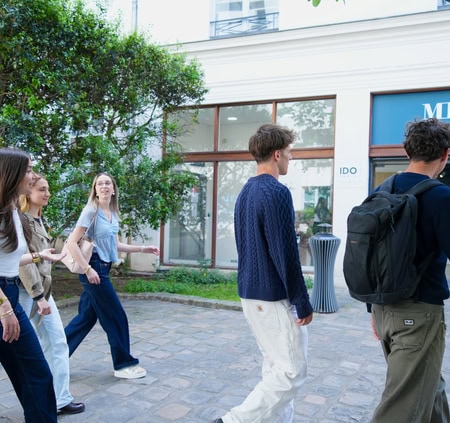 Jeunes piétons en groupe marchant rue ensoleillée devant vitrines à Paris.