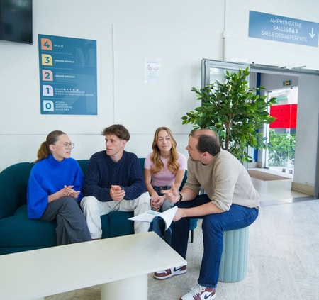 Groupe en réunion informelle dans un espace dattente lumineux, canapé, documents et plante.
