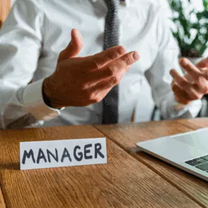 Un homme est assis à son bureau, devant lui il y a un chevalet avec écrit Manager dessus.