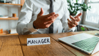 Un homme est assis à son bureau, devant lui il y a un chevalet avec écrit Manager dessus.