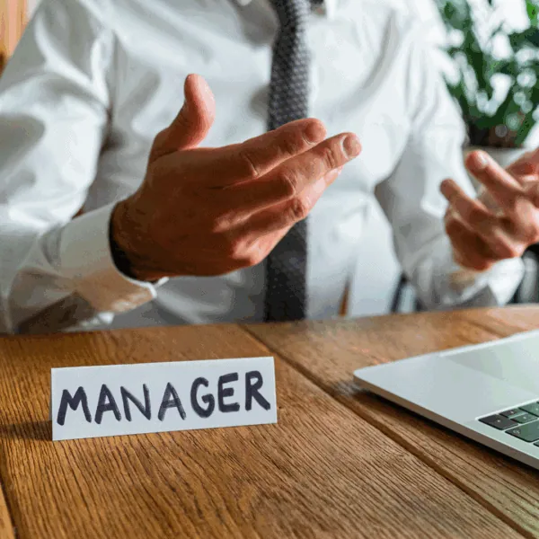 Un homme est assis à son bureau, devant lui il y a un chevalet avec écrit Manager dessus.