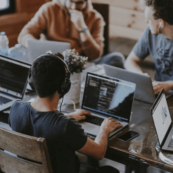 Des jeunes travaillent autour d'un bureau, avec leurs ordinateurs ouverts.