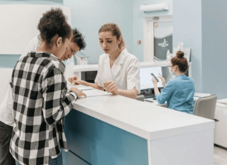 Un couple dans un centre médical demandant des informations à une femme derrière un comptoir