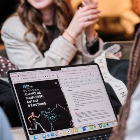 Ordinateur portable écran partagé, collaboration et télétravail, femme en arrière‑plan floue.