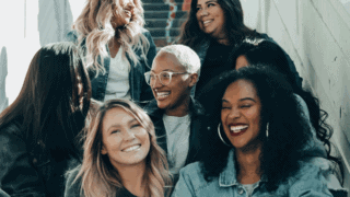 Un groupe de femmes assises sur des escaliers sourient toutes ensemble.