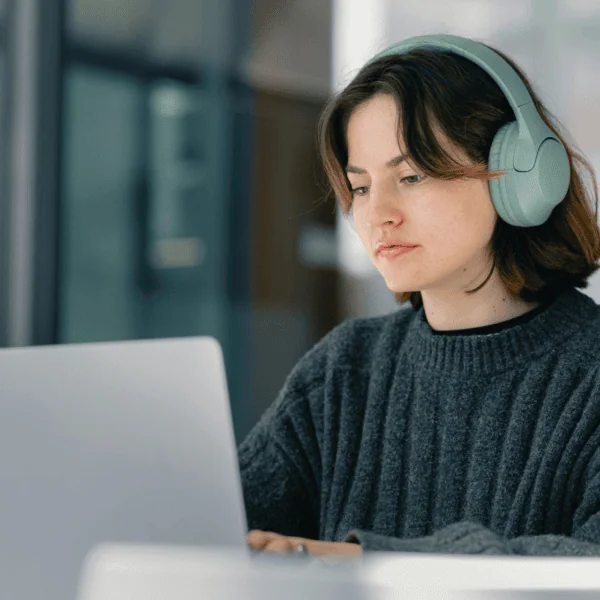 Femme concentrée portant casque, travaillant sur ordinateur portable en bibliothèque moderne.
