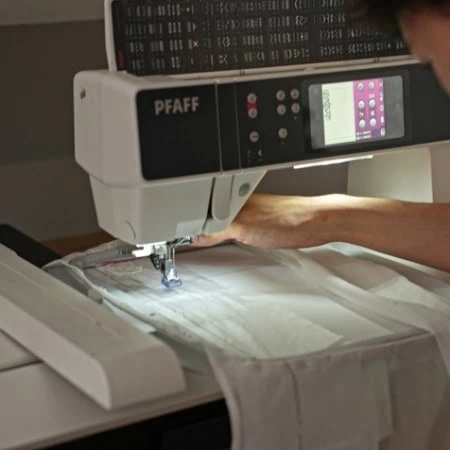 Machine à coudre industrielle en atelier, mains guidant tissu texturé doré, couture artisanale.