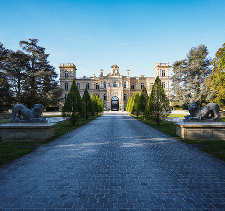 Manoir symétrique en pierre avec allée pavée, bassins réfléchissants et jardins formels.