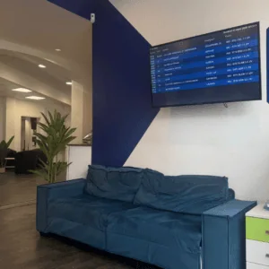 Accueil et salle dattente moderne avec canapé bleu, écran daffichage et plantes.