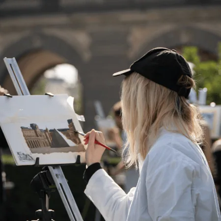Artiste peignant en plein air à laquarelle sur chevalet devant arcades architecturales.