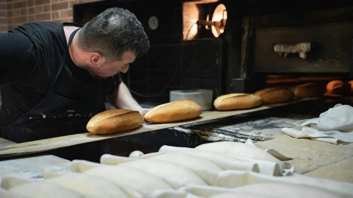 Boulanger artisanal surveillant cuisson de pains dorés au four traditionnel.