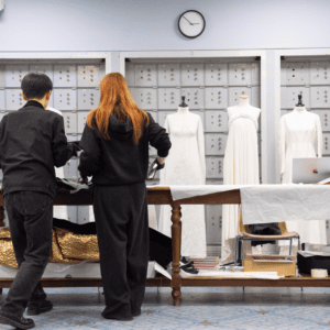 Atelier de conservation textile: deux restaurateurs examinant vêtements historiques sur mannequins.
