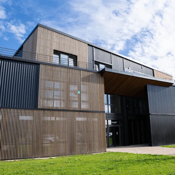 Bâtiment moderne trois étages avec bardage bois et métal, fenêtres et terrasse.