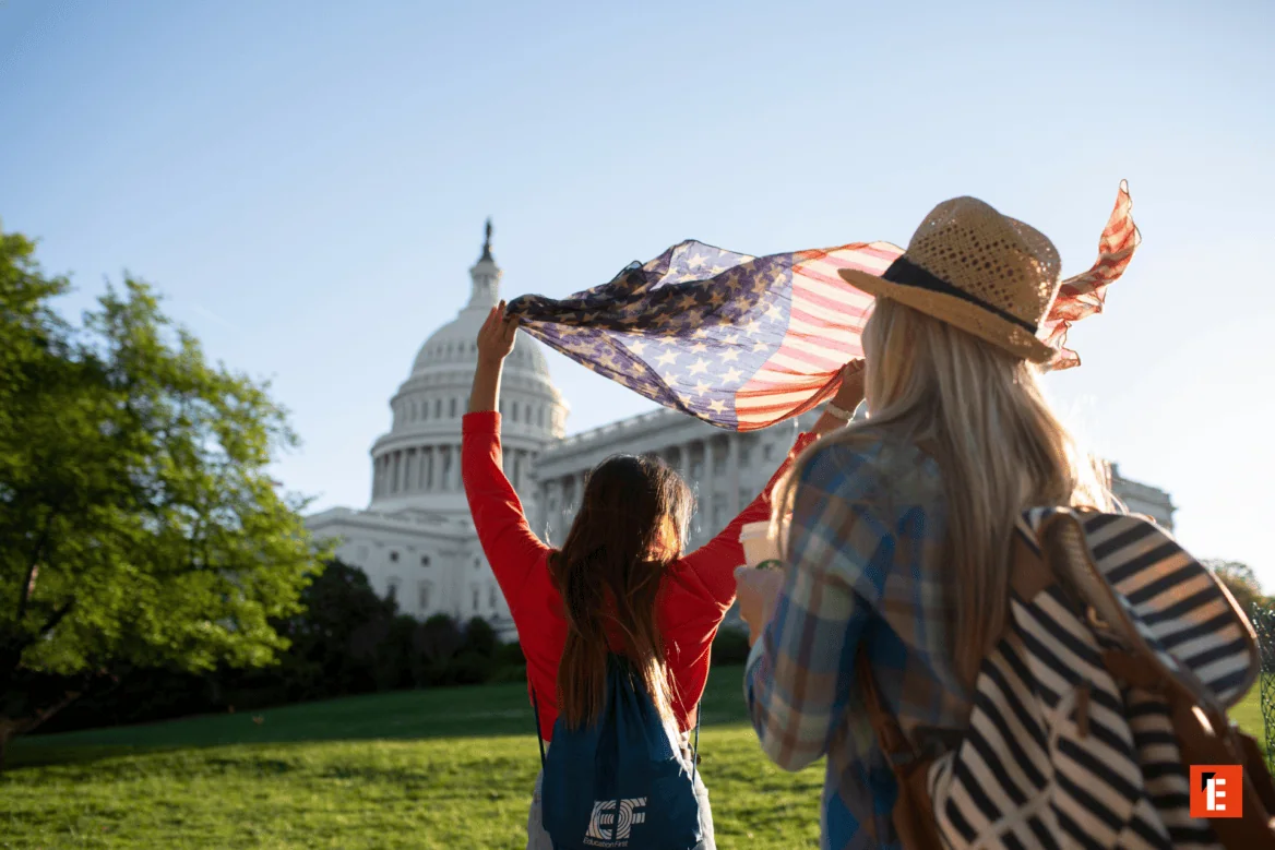 Jeunes touristes avec drapeau américain devant le Capitole de Washington au coucher de soleil.