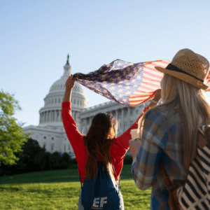 Jeunes touristes avec drapeau américain devant le Capitole de Washington au coucher de soleil.