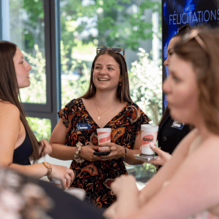 Groupe de jeunes adultes souriants en conversation lors dune réception conviviale avec tasses et badges.