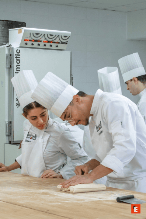 Chefs pâtissiers en atelier façonnant pâte feuilletée sur table farinée.