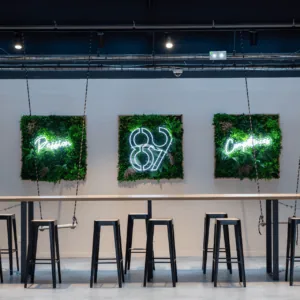 Comptoir commun design minimaliste avec néons, murs végétalisés et tabourets noirs.